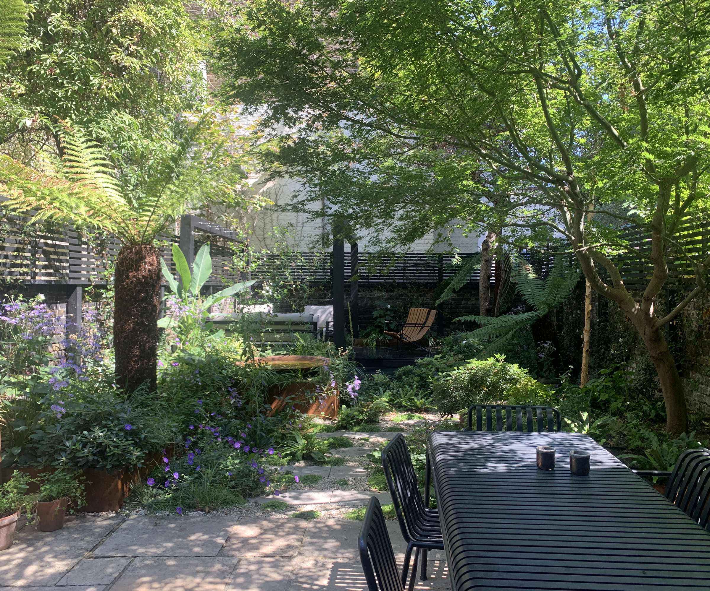 A small rectangular garden in an urban plot. With an outdoor dining table near the house and a relaxed seating area at the rear