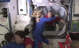 Astronaut Soichi Noguchi is greeted by astronaut Kate Rubins as he enters the International Space Station from the vestibule between the SpaceX Dragon capsule and the ISS.