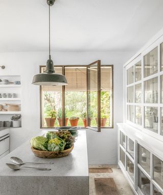 white kitchen with iron frame window, white glazed cabinets, gray stone island and enamel pendant light