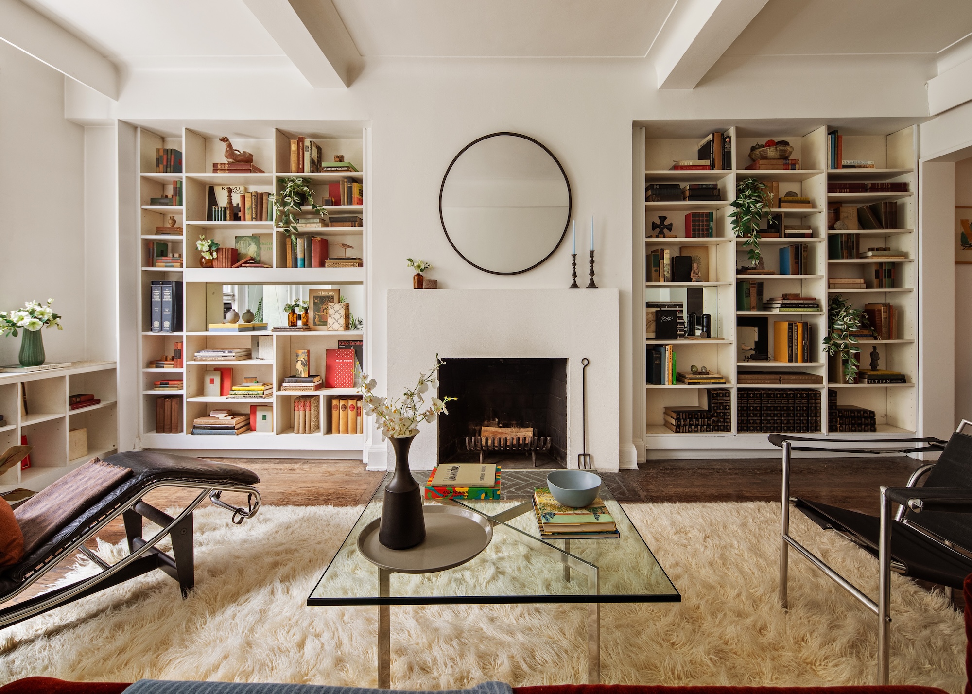 A traditional, yet modern living room in an off white with a central fireplace and built in shelvingon both sides, and modern furniture and glass coffee table set back from the fireplace.
