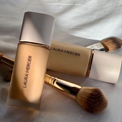 Two bottles of Laura Mercier Real Flawless Weightless Perfecting Foundation piled up with two foundation brushes