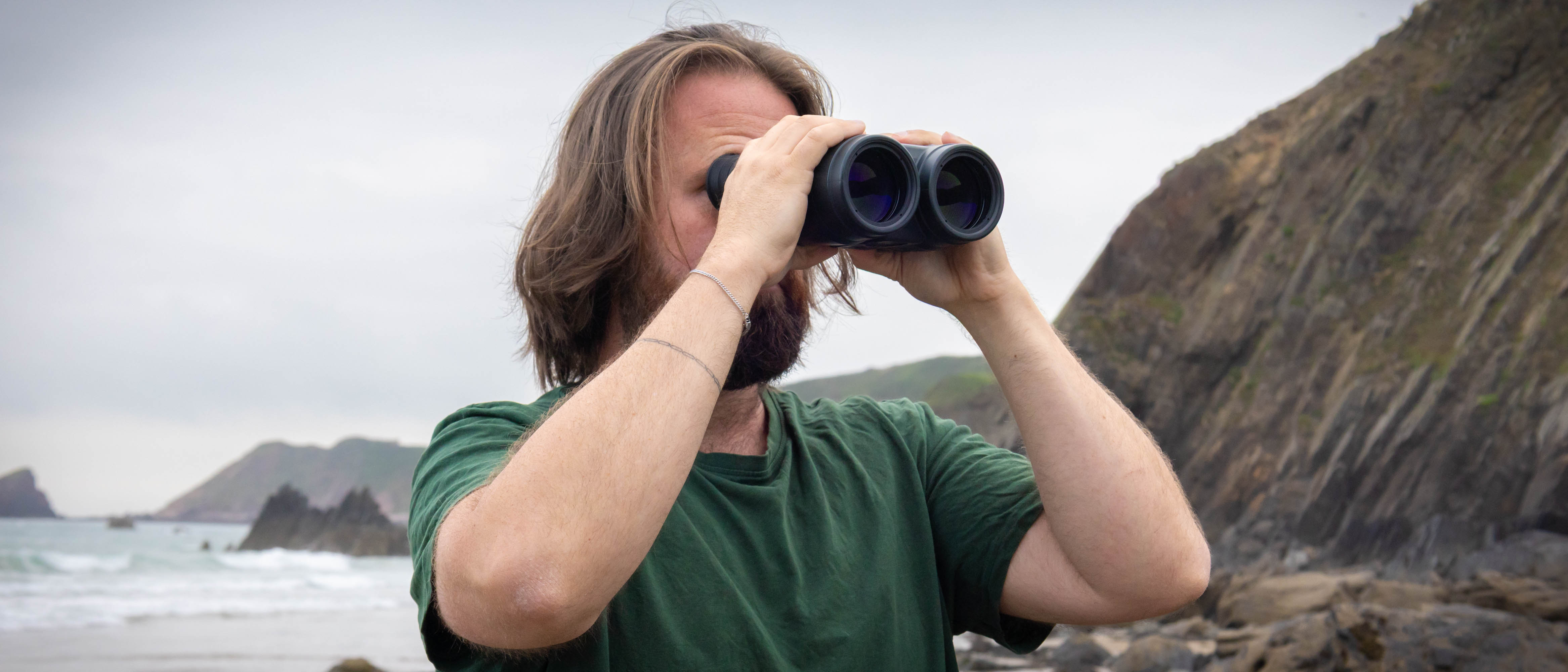 A male using the Canon 18x50 IS binoculars with the sea and coastline behind them.