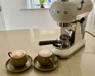 Smeg espresso machine in white on kitchen counter with two mugs of coffee