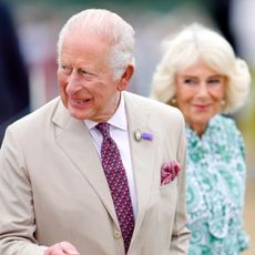 King Charles wears a light tan suit and carries a wooden walking stick while attending the RHS Sandringham Flower Show
