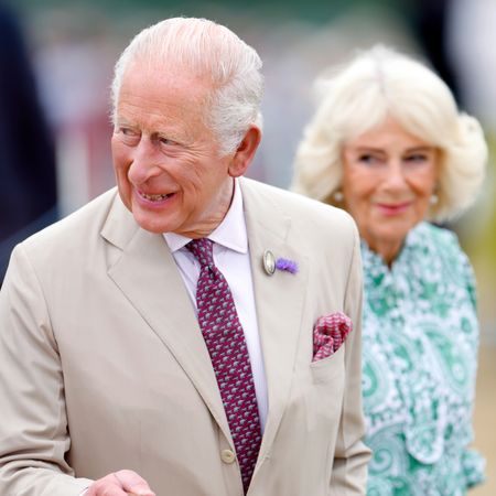 King Charles wears a light tan suit and carries a wooden walking stick while attending the RHS Sandringham Flower Show