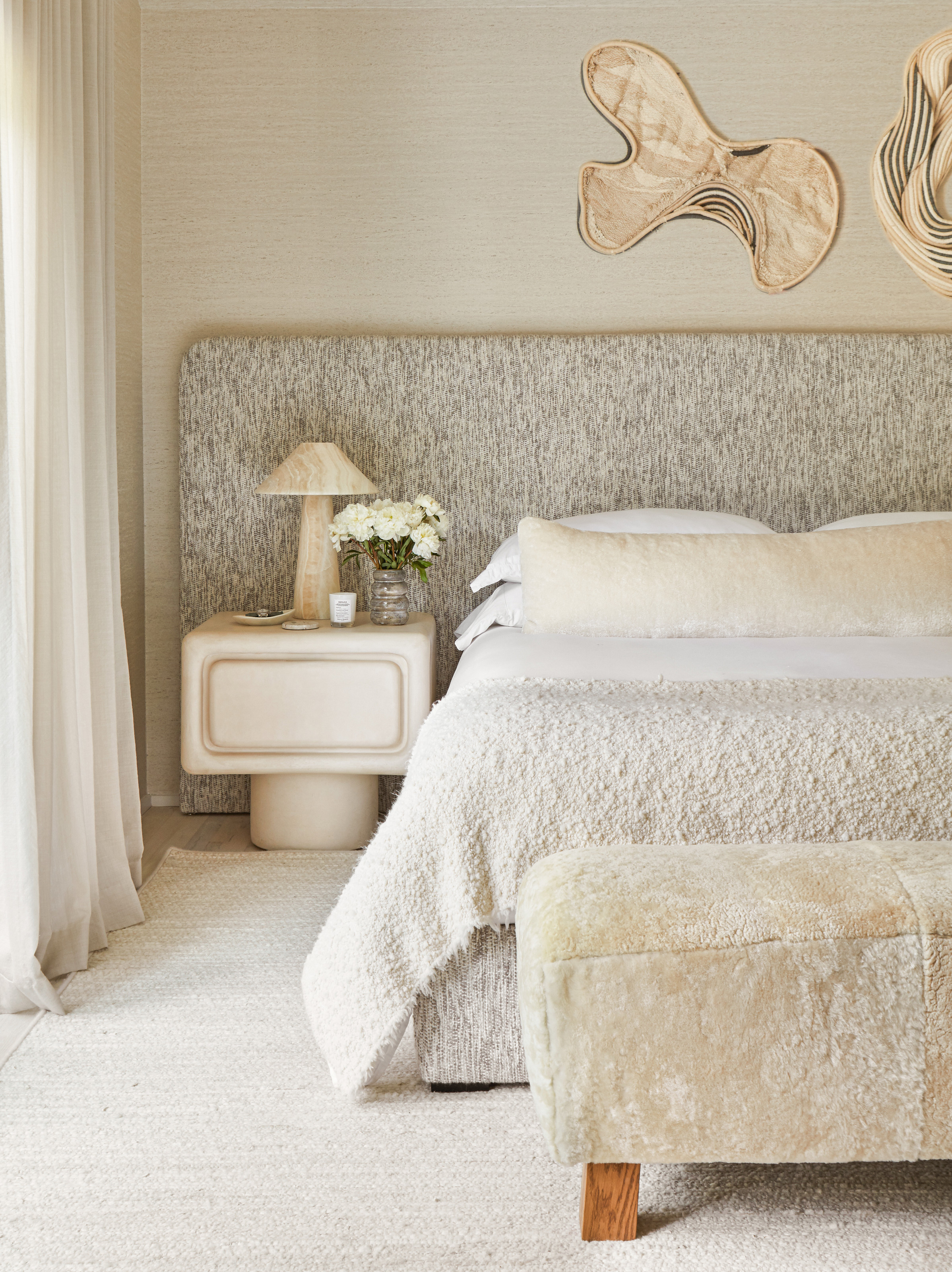 Bedroom with grey oversized headboard, white textured throw, white bedside table and abstract wall art