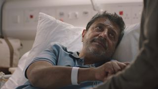 Ravin J. Ganatra as Kareem in a hospital bed holding Rash's hand.