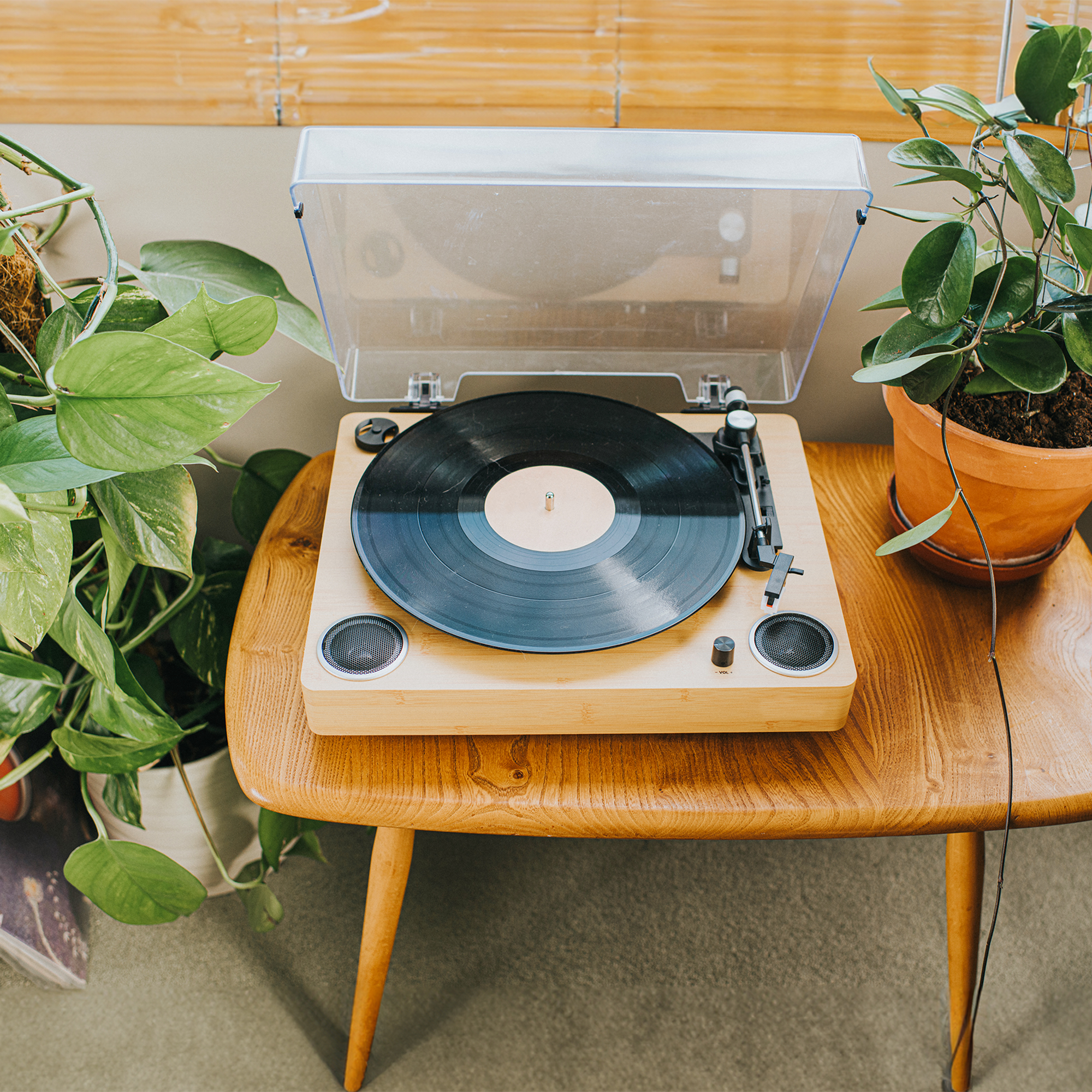 Elevated view of a modern record player on a wooden table. A potted plant sits to one side.
