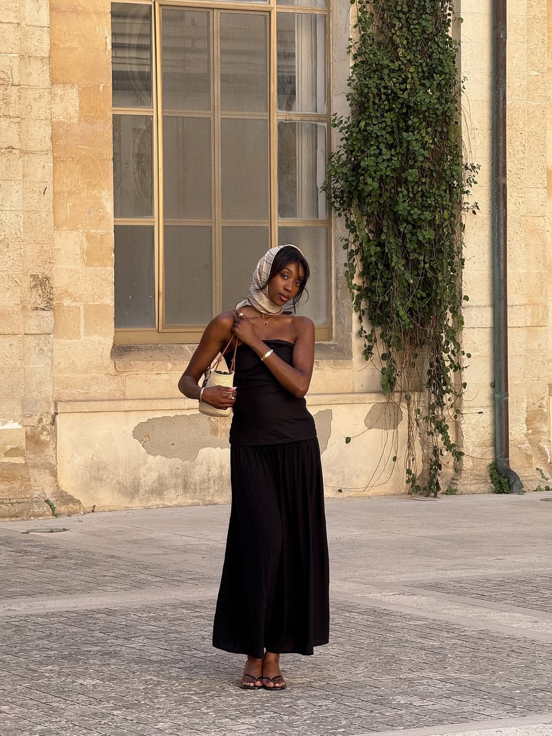 @emmanuellek_ wears a monochrome silk scarf with a black bandeau maxi dress, basket bag and mules