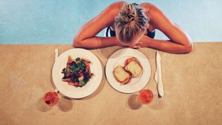 A woman in a pool with plates of food and drink by her