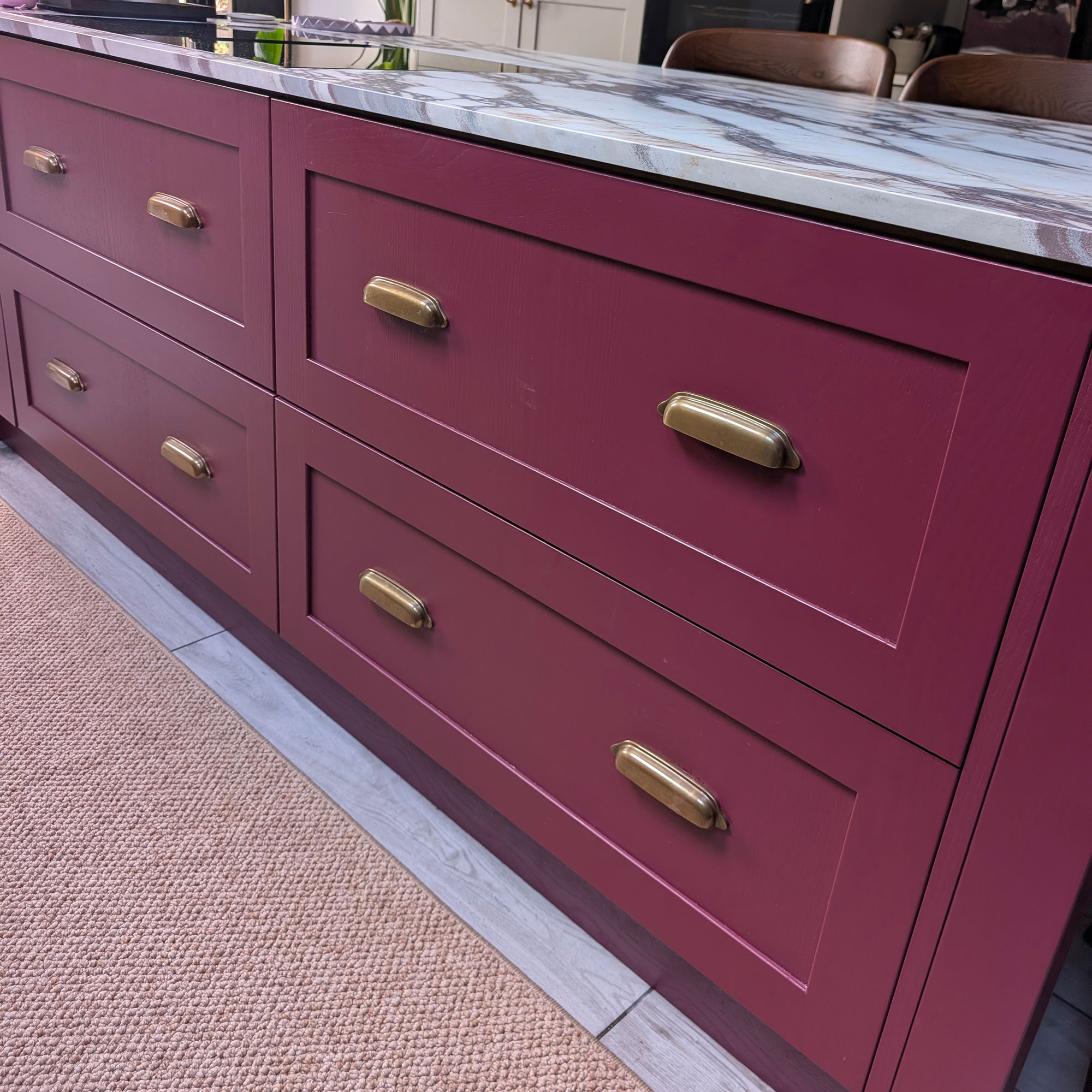 Kitchen island with red cabinetry, marble top and brass pulls with sisal style runner on floor beside