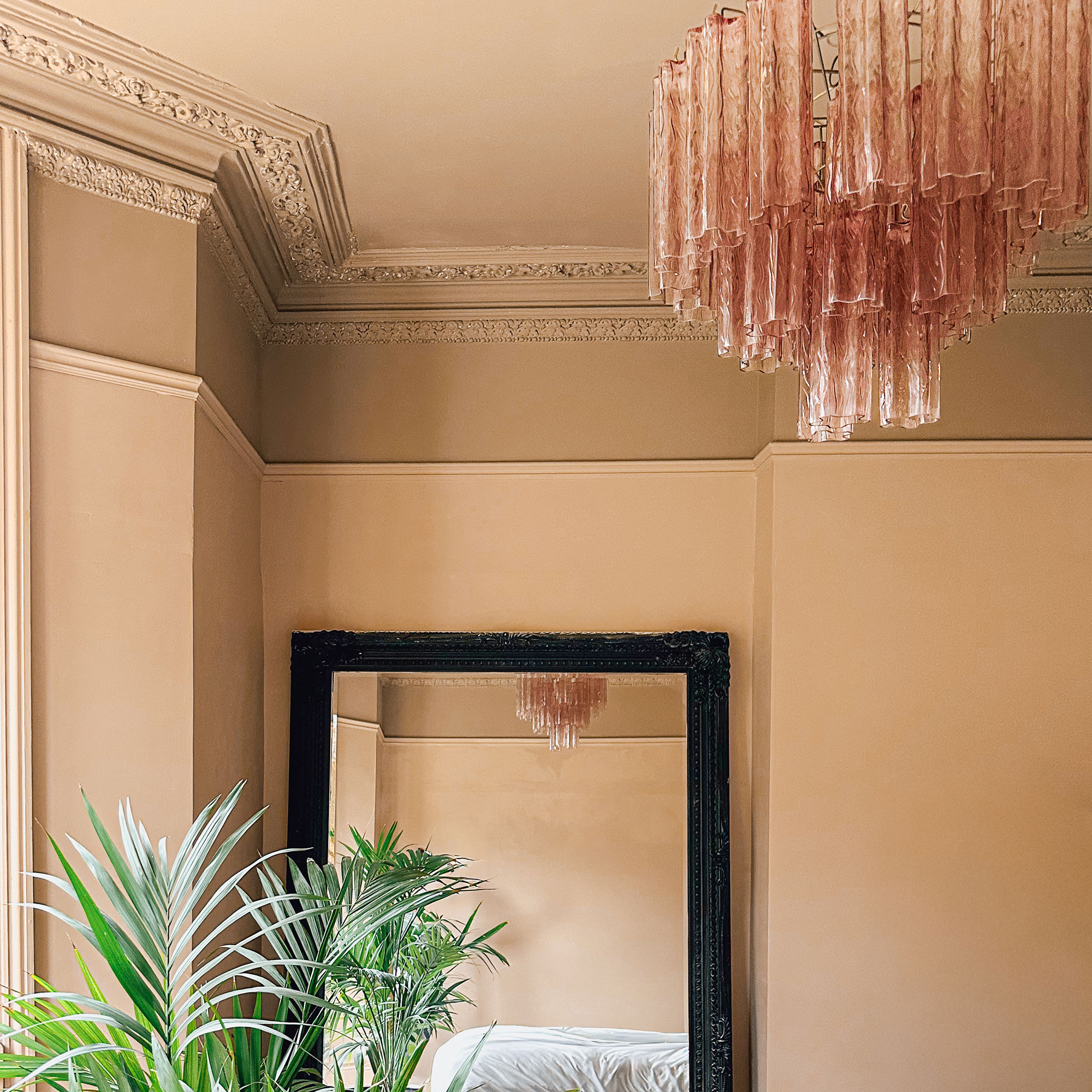 Pink glass chandelier in bedroom with peach walls, full length mirror and palm style plant