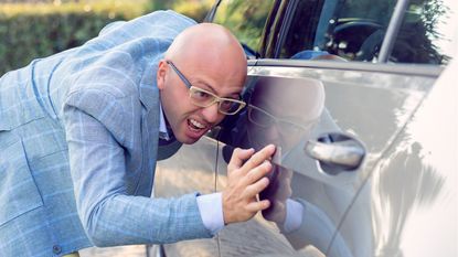 A man looks distressed by a very small scratch on his car.