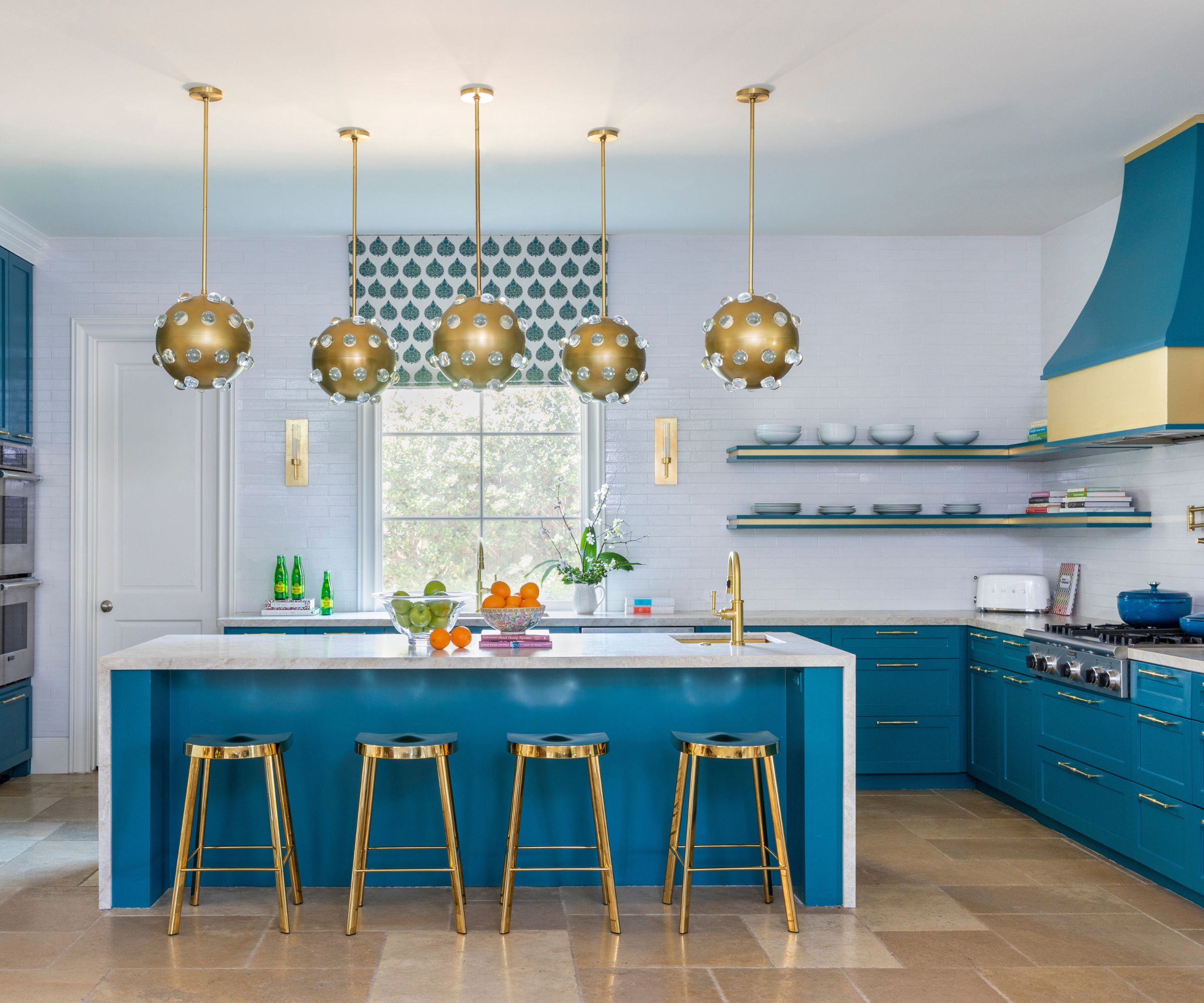 Blue kitchen with gold pendant ceiling lamps over a kitchen island inspired by 1970s glamour