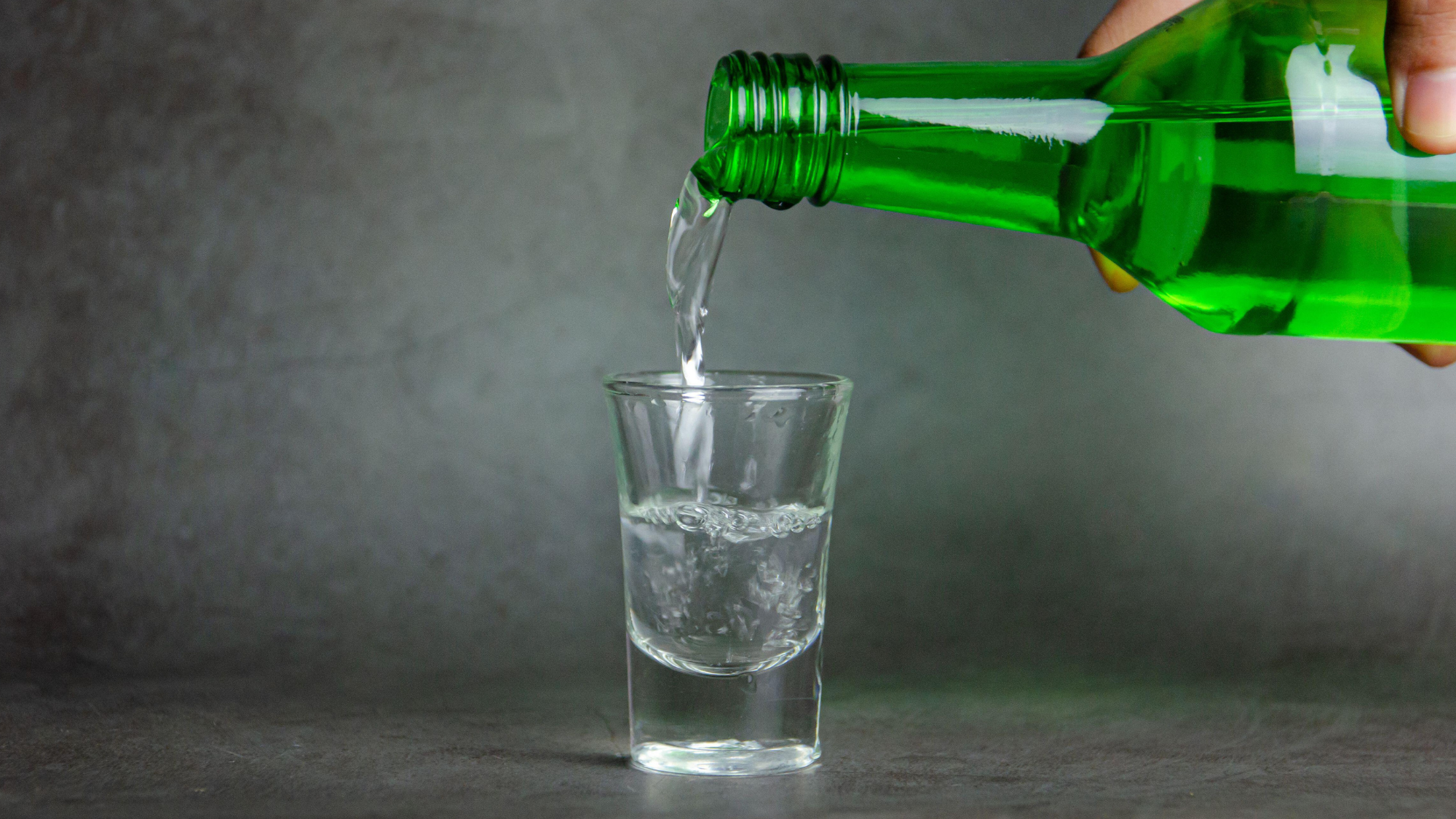 A green bottle of soju being poured into a shot glass.