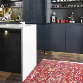 Navy kitchen with white island worktop and red antique-style rug.
