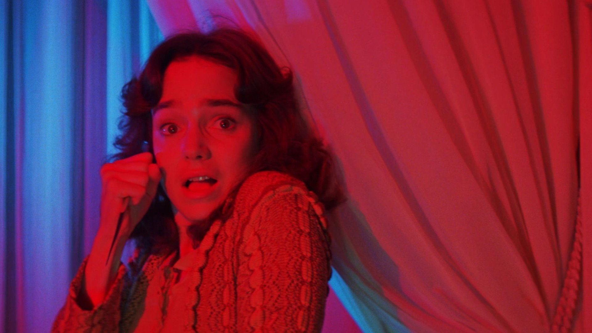 Jessica Harper jako Suzy Bannion trzymająca nóż w pokoju z czerwonym oświetleniem podczas horroru Suspiria.