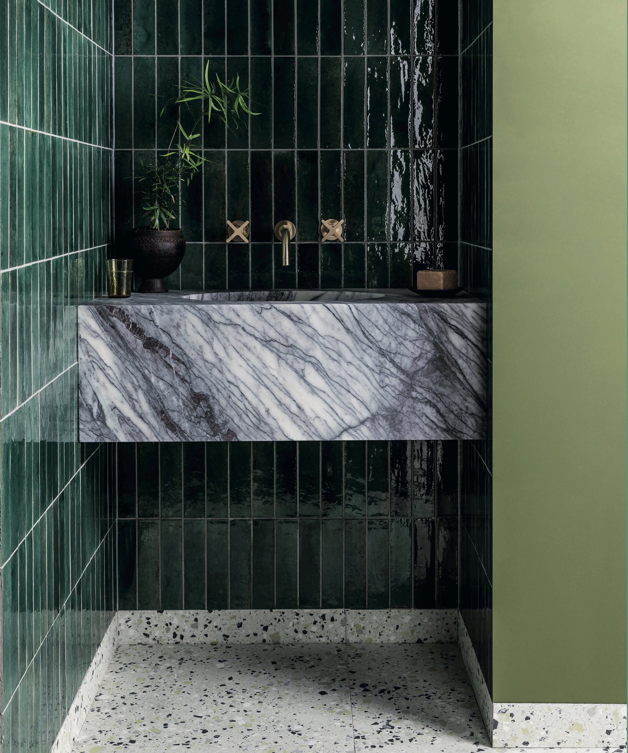 A marble basin in a bathroom with dark green wall tiles