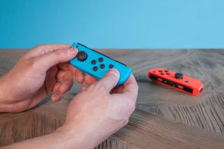 A person holding a blue Nintendo Switch Joy-Con in their hands with a red Joy-Con in the background