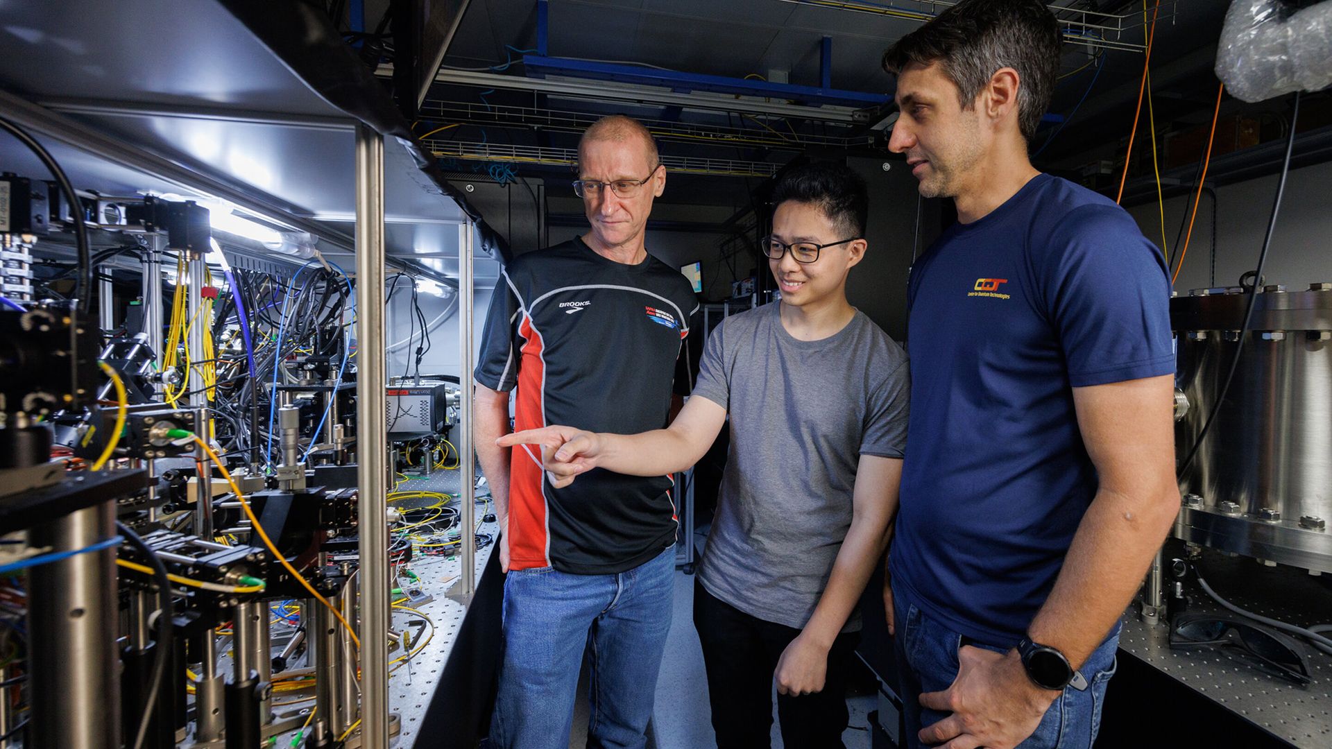 Three men stand next to a laser table with machinery on it.