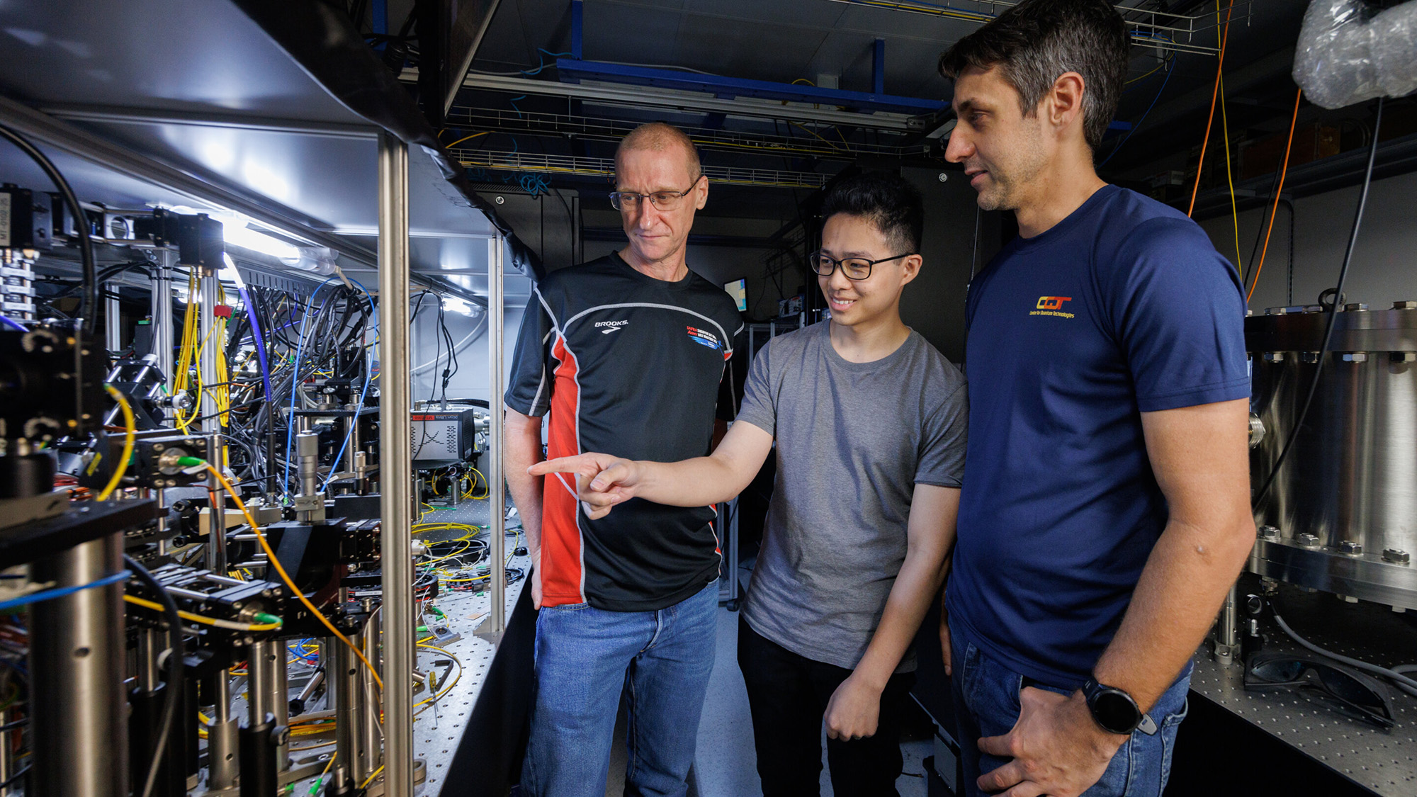 Three men stand next to a laser table with machinery on it.
