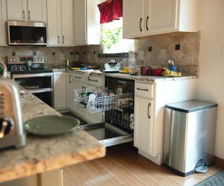 A cluttered middle class suburban kitchen with silver toaster and silver trash can