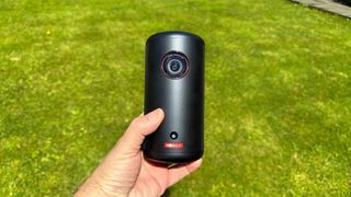 Anker Nebula Capsule 3 portable projector held in hand over grassy lawn