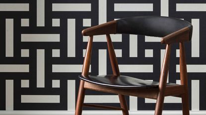 Black and white geometric wallpaper in room with one mid-century style chair upholstered in black leather