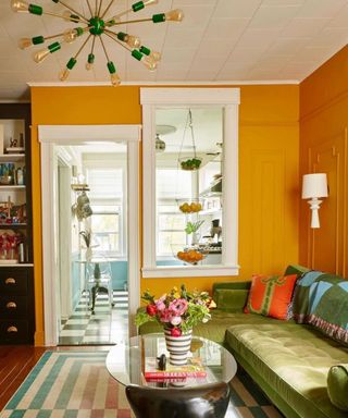 A living room with yellow walls, a white ceiling, a colorful rug, green couch, and a coffee table with decor on it