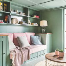 A seating nook with shelving above, all drenched green, with pink blankets and cushions