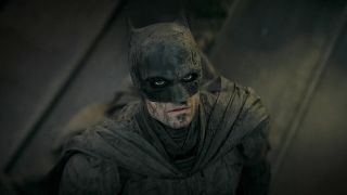 The Batman, as played by Robert Pattinson, looking up with hope, covered in ash and dust. 