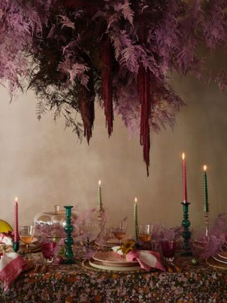 Pink and burgundy floral arrangement suspended over a dining table set up for a Christmas meal