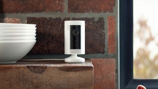 Ring indoor cam security camera on a shelf in a kitchen with an exposed brick wall