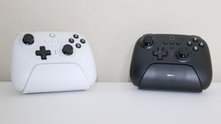 The 8BitDo Ultimate Controller in white and black with charging dock next to each other