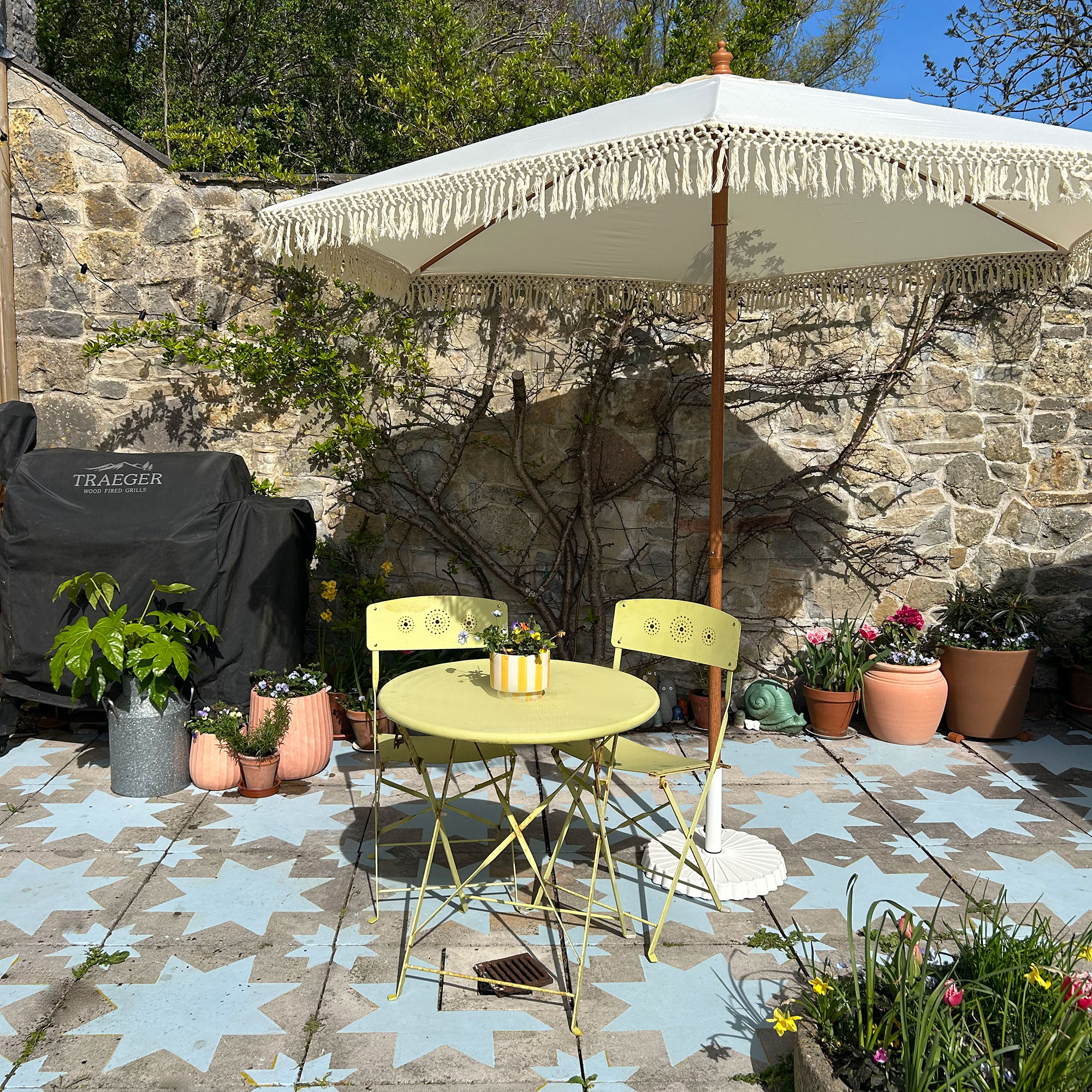 Patio with yellow bistro set, macrame parasol, potted plants and slabs painted with blue star design