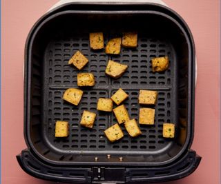 Tofu in an air fryer drawer on a rose background