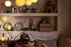 alcove shelving with ornaments and presents wrapped in plain brown wrapping paper with part of a table in view with a platter of food a bottle of wine and some blurred twinkling lights setting the minimalist Christmas scene