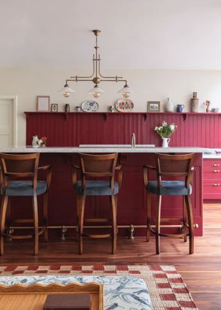 beadboard kitchen cabinets in red with bar stools placed by a kitchen island and red back panelling running across the kitchen.