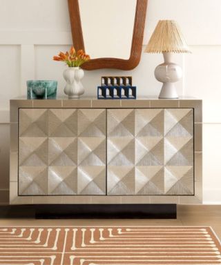 A gold and white rug on a floor next to a metallic console table with decor on it