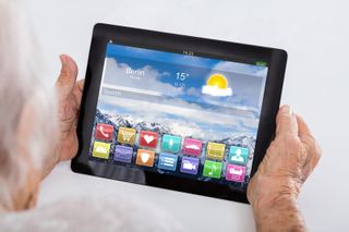 Ein Tablet wird von einer älteren Person gehalten, man sieht die verfügbaren Apps