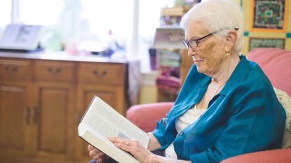 A woman reads a book in her nursing home room.