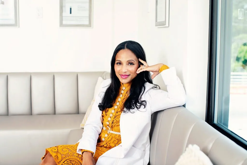 an Indian woman with dark hair in a white lab coat and gold dress