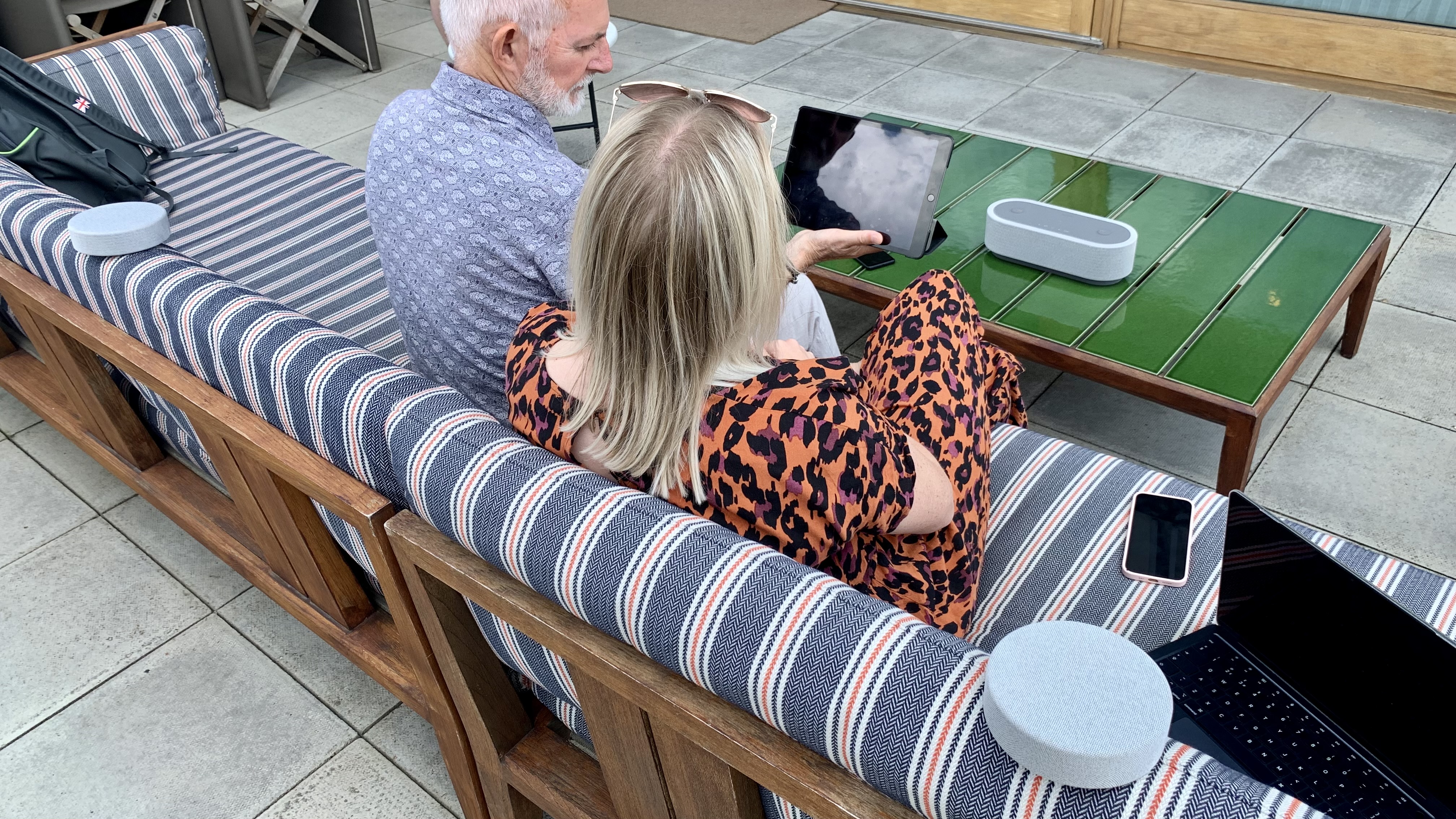 Der Sony HT-AX7 wird auf einem Balkon im Klangfeldmodus von einem Mann und einer Frau benutzt, die Harry Stiles auf einem iPad hören.