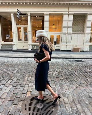 Eliza Huber wearing a cream Mains de Vapeur hat with a navy blue Emilia Wickstead dress, black bag, and black heels in SoHo.