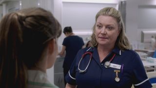 Laurie Brett as midwife Maria in a navy blue uniform with white trim on the sleeves and a red stethoscope around her neck talking to Jodie.