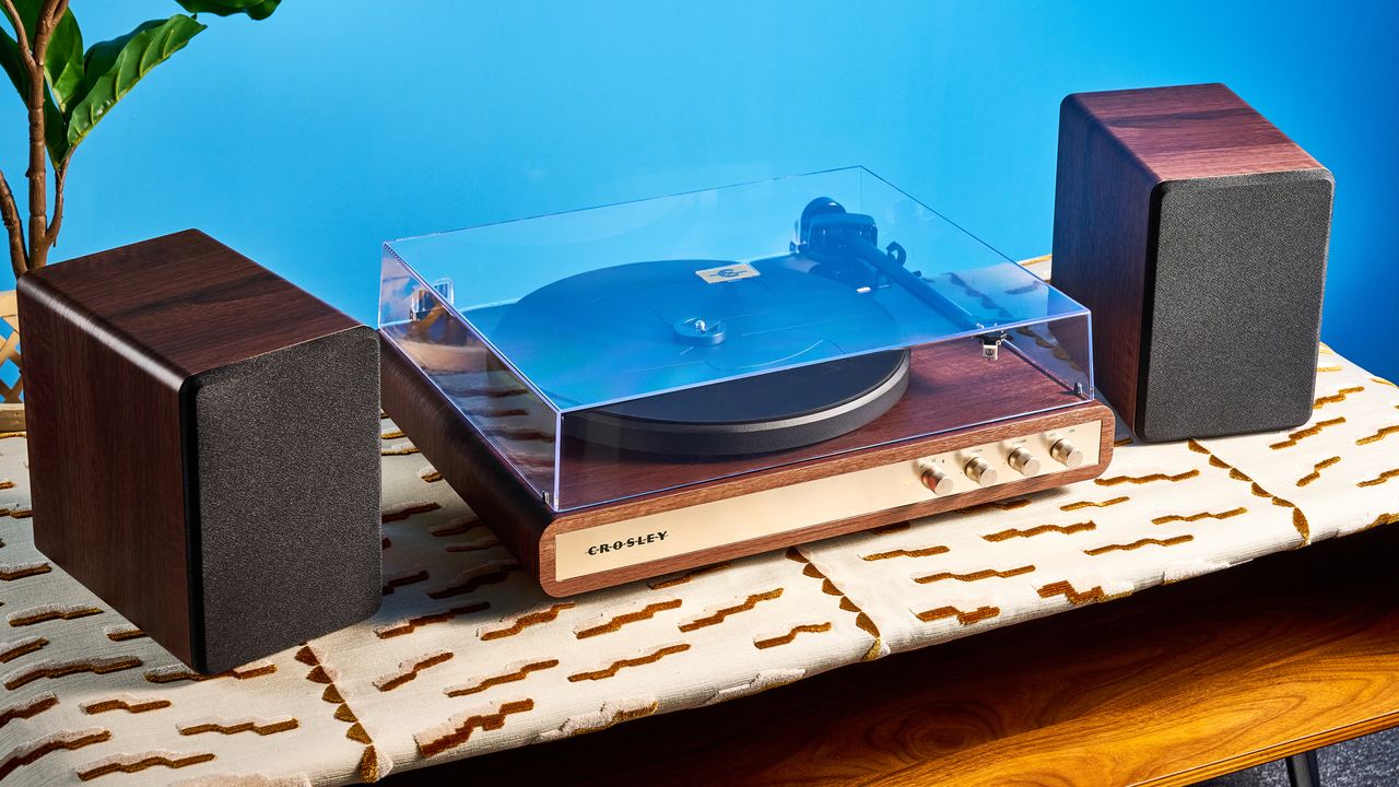 Crosley C65 turntable and bookshelf speakers photographed in front of a blue background on a brown table.