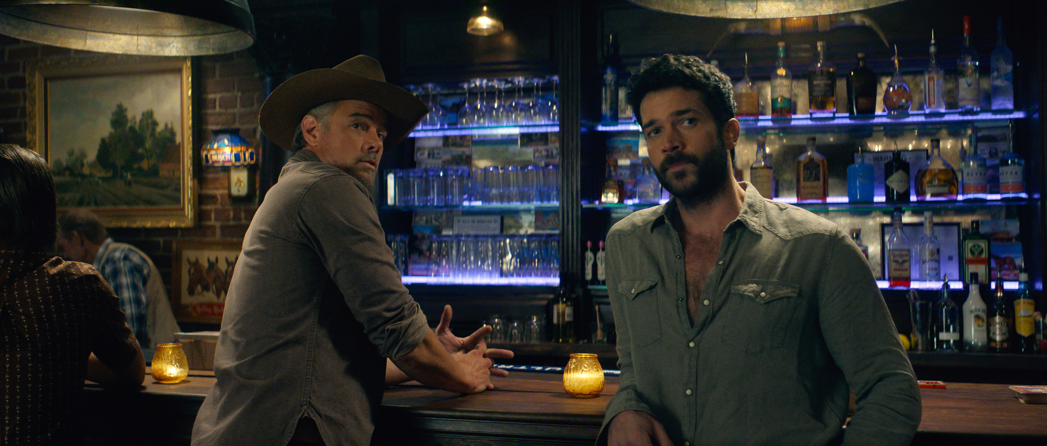 Josh Duhamel as Staten and Jack Schumacher as Yancy sitting at a bar looking to their right in a still from ransom canyon season 2