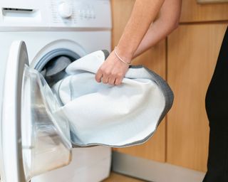 person putting grey fabric into a washing machine