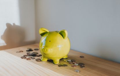yellow piggy bank on a wooden tabletop with coins spread around it