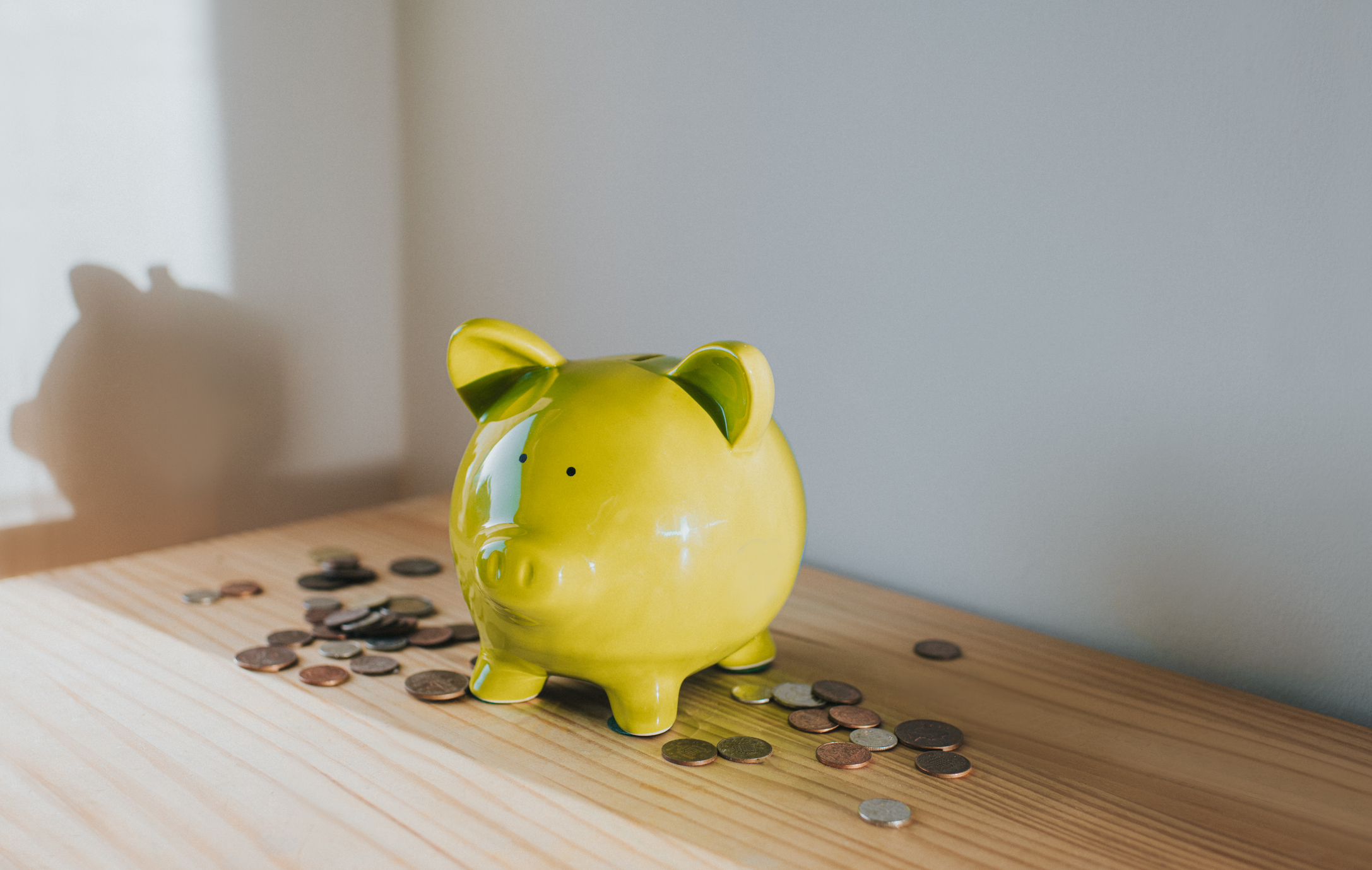 yellow piggy bank on a wooden tabletop with coins spread around it
